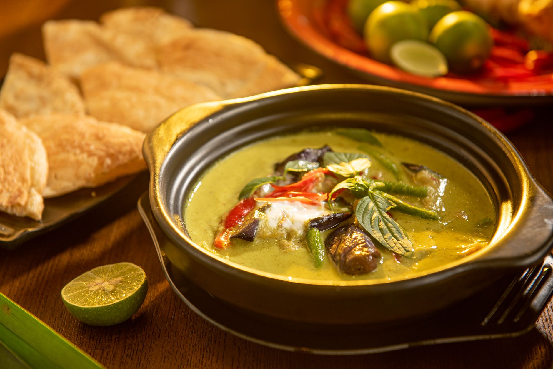 Thai green curry in a ceramic bowl with fresh herbs and lime